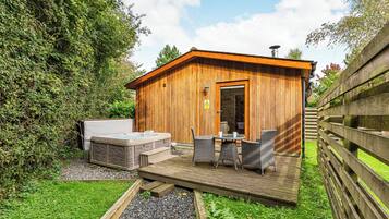 A wooden cabin with a hot tub, outdoor seating, and a gravel pathway.