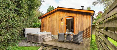 Een houten hutje met een jacuzzi, buitenzitplaatsen en een grindpad.