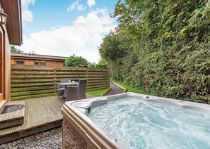 A hot tub with a wooden deck, wicker furniture, and a wooden fence. - Semi-detached deluxe lodge offering the perfect romantic retreat. (Cartmel)