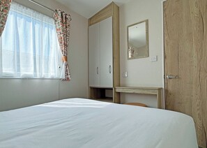 A bedroom with a bed, a wardrobe, a desk, and a mirror.