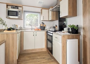Una cocina compacta con armarios de madera, microondas, estufa y pileta.