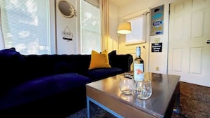 A living room with a dark blue sofa, a small coffee table with a bottle and glasses, and a lamp. There are wall decorations including a fish poster and a sign that says "Life is better at the lake." - 3-bedroom vacation home just a short walk to Lake Michigan (Racine)