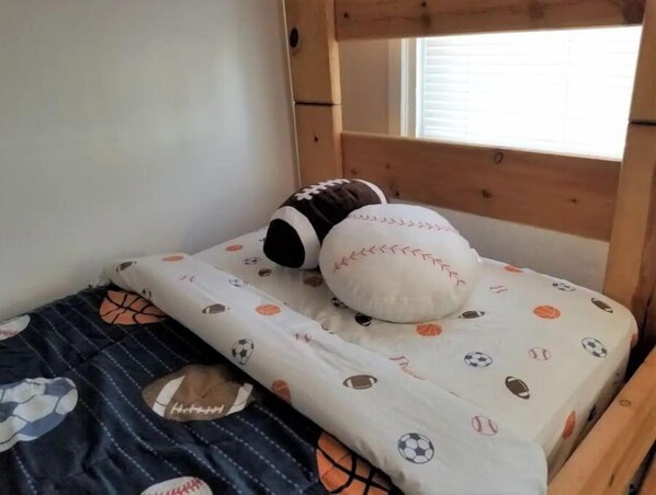 A bed with a white mattress featuring a sports-themed pattern, a dark blue blanket with a soccer ball design, and two pillows, one with a baseball design and the other with a basketball design. - 3-bedroom vacation home just a short walk to Lake Michigan (Racine)