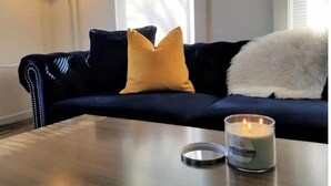 A dark blue sofa with a white fluffy throw and a mustard yellow pillow. A lit candle is on a table in front of the sofa. - 3-bedroom vacation home just a short walk to Lake Michigan (Racine)
