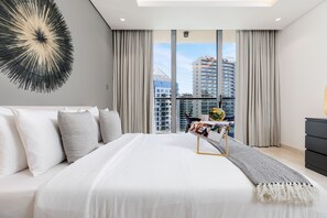 Une chambre moderne avec un grand lit, une vue sur la ville et une petite table sur laquelle est posé un plateau.
