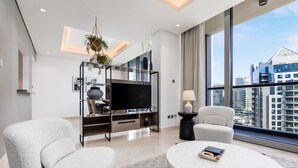 Una sala moderna con un televisor de pantalla plana, dos sillones cómodos, una mesa redonda y un amplio ventanal con vistas a la ciudad.