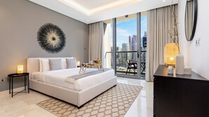 Una habitación de hotel moderna con una cama grande, una mesita auxiliar pequeña, un adorno en la pared, un balcón con vistas a la ciudad y un espejo grande.