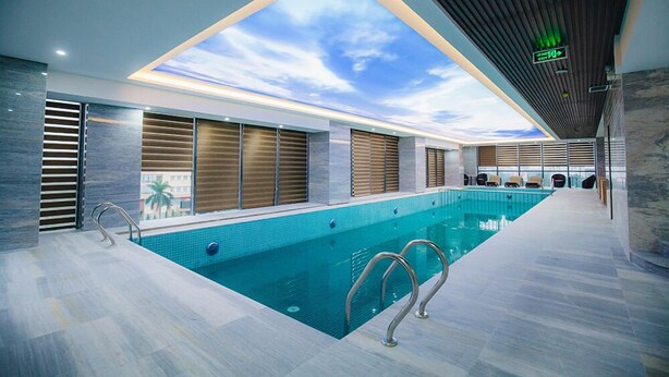 Una piscina interior con techo de tragaluces, barandillas de metal y vistas a palmeras al exterior.