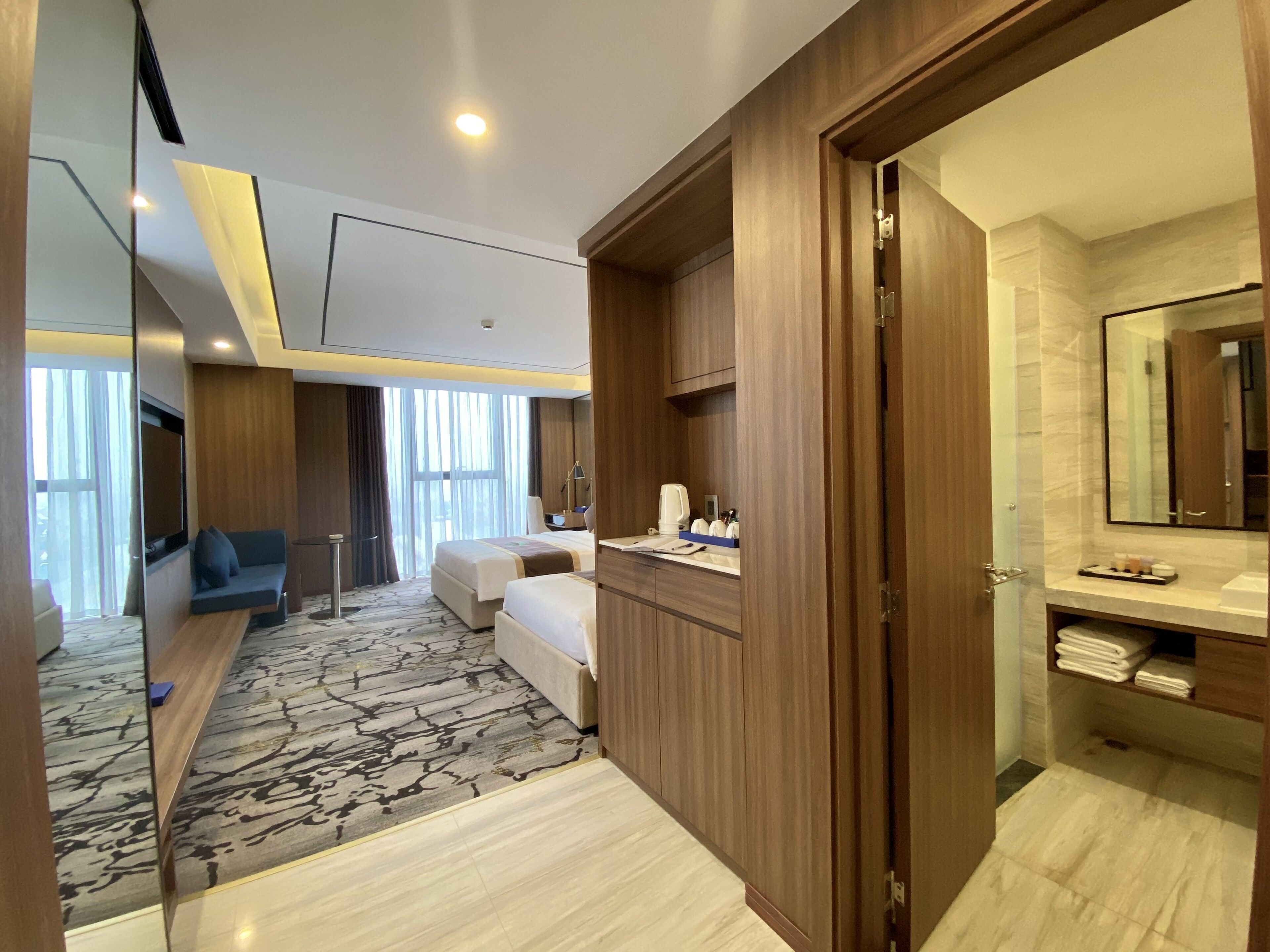 A hotel room with a bed, a seating area, a desk, a bathroom with a mirror, and a view of the outdoors.