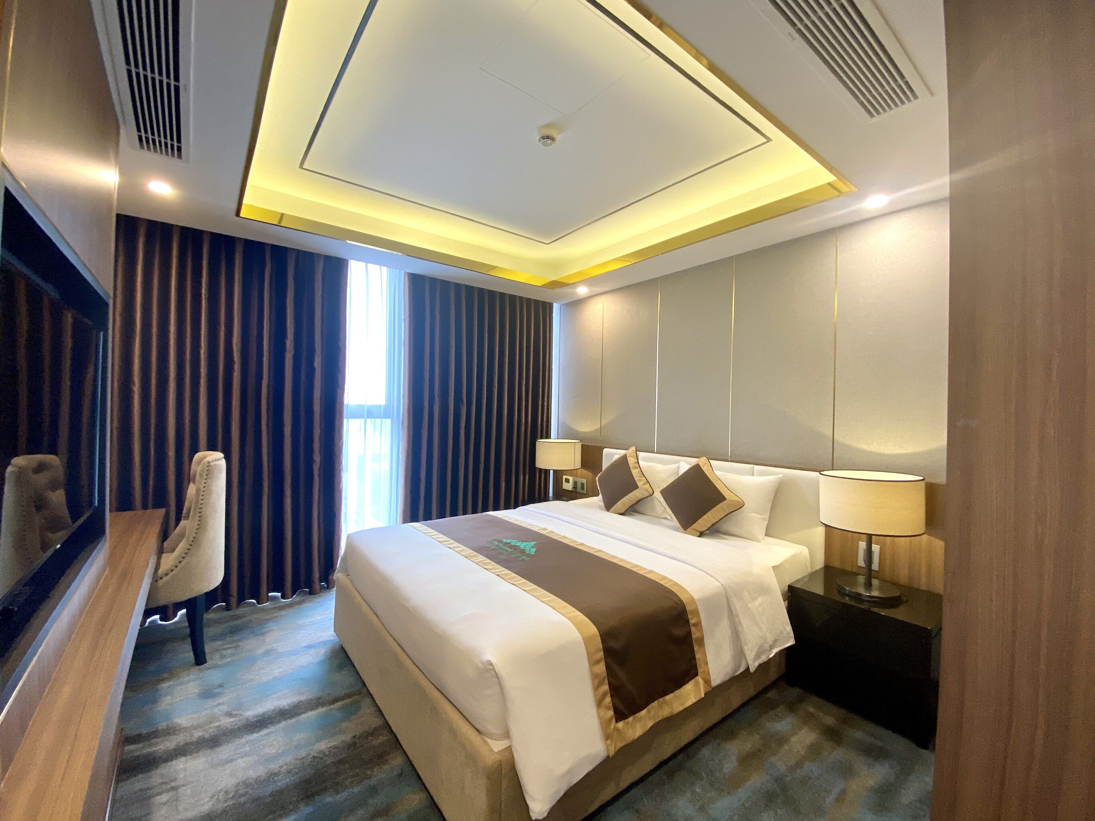 Quarto de hotel com uma cama grande, escrivaninha, cadeira e televisão.