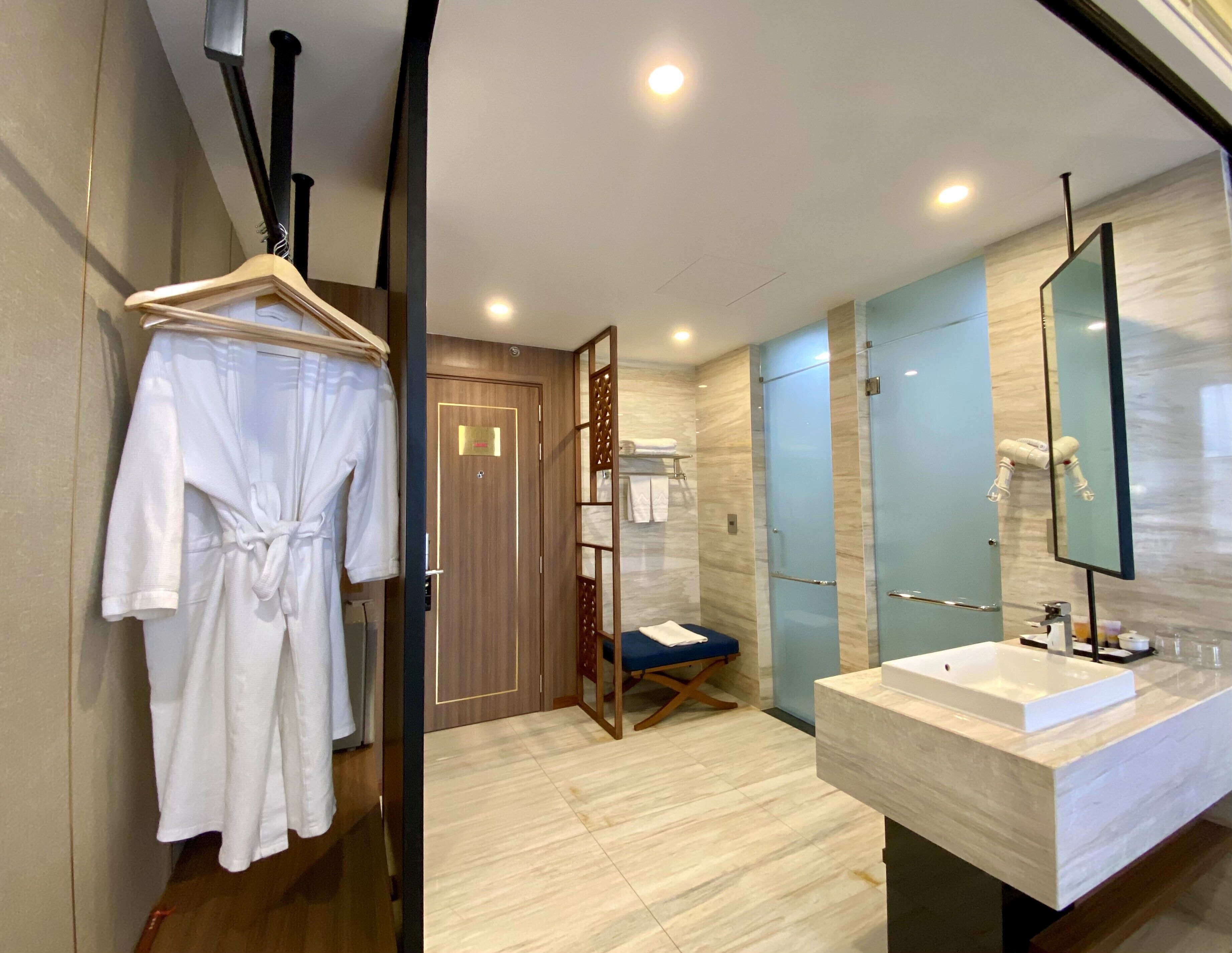 A modern bathroom with a large mirror, a sink, and a robe hanging on a rack.