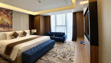 Una habitación de hotel con una cama grande, un sofá azul, un televisor de pantalla plana y una alfombra estampada.