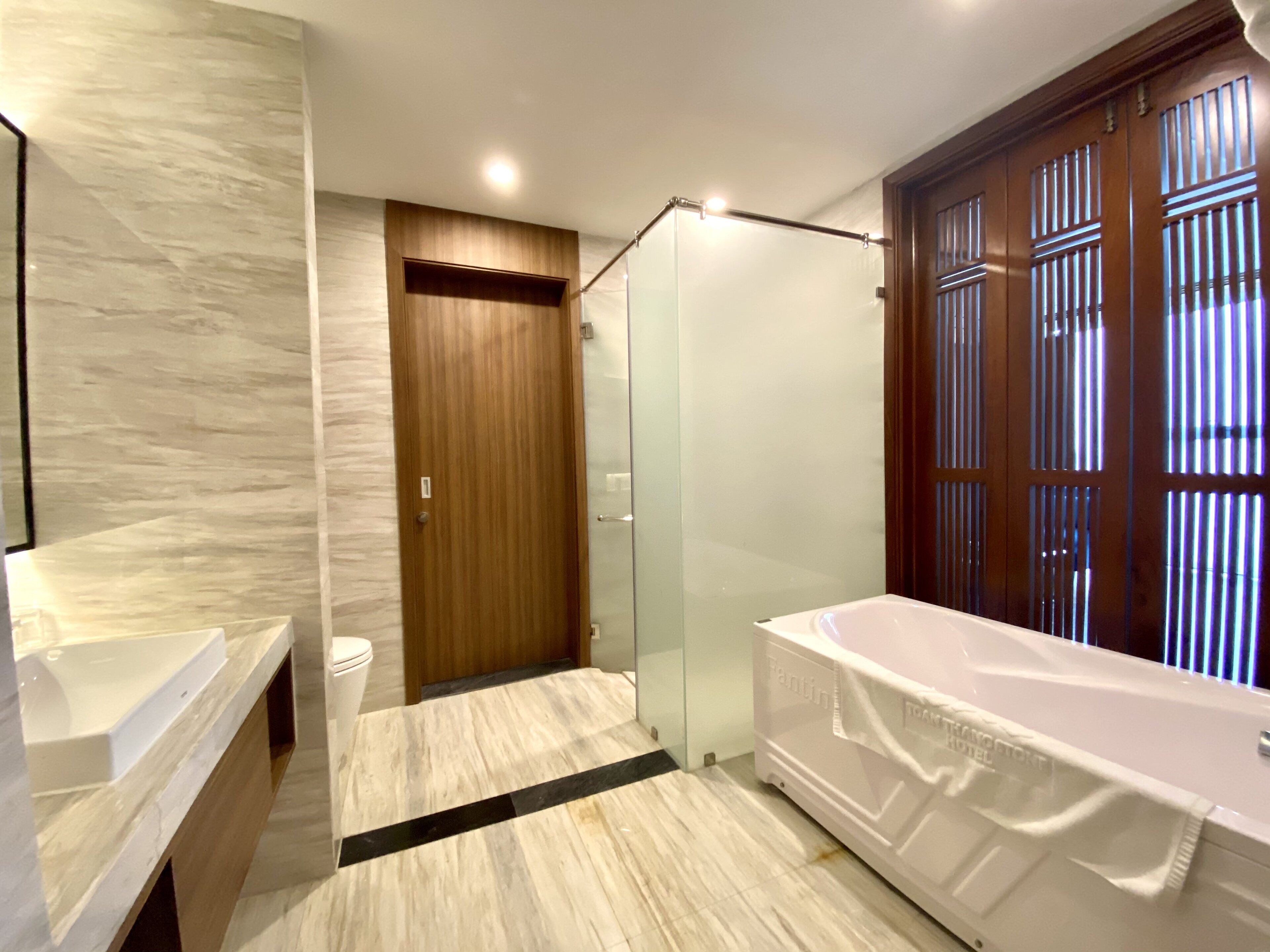 Ein modernes Badezimmer mit Marmorboden, Holztür, Duschkabine aus Glas und einer weißen Badewanne.