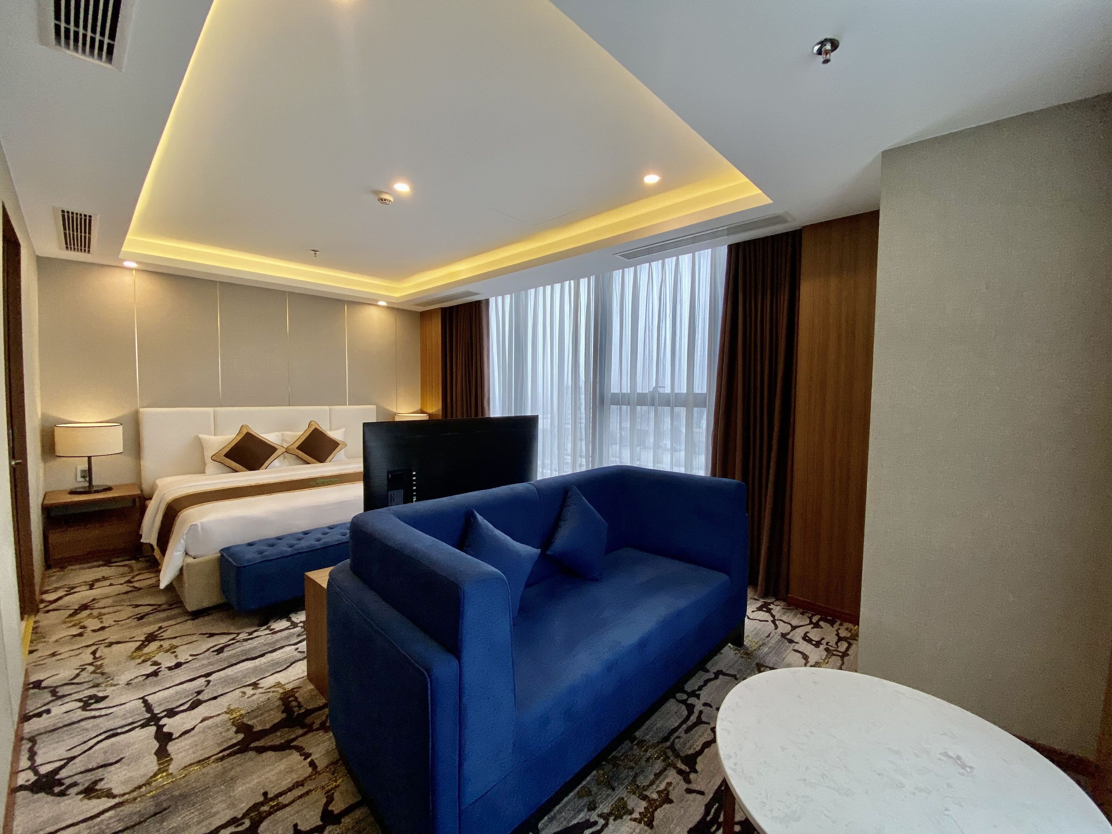 A hotel room with a bed, a blue sofa, a TV, and a window with curtains.
