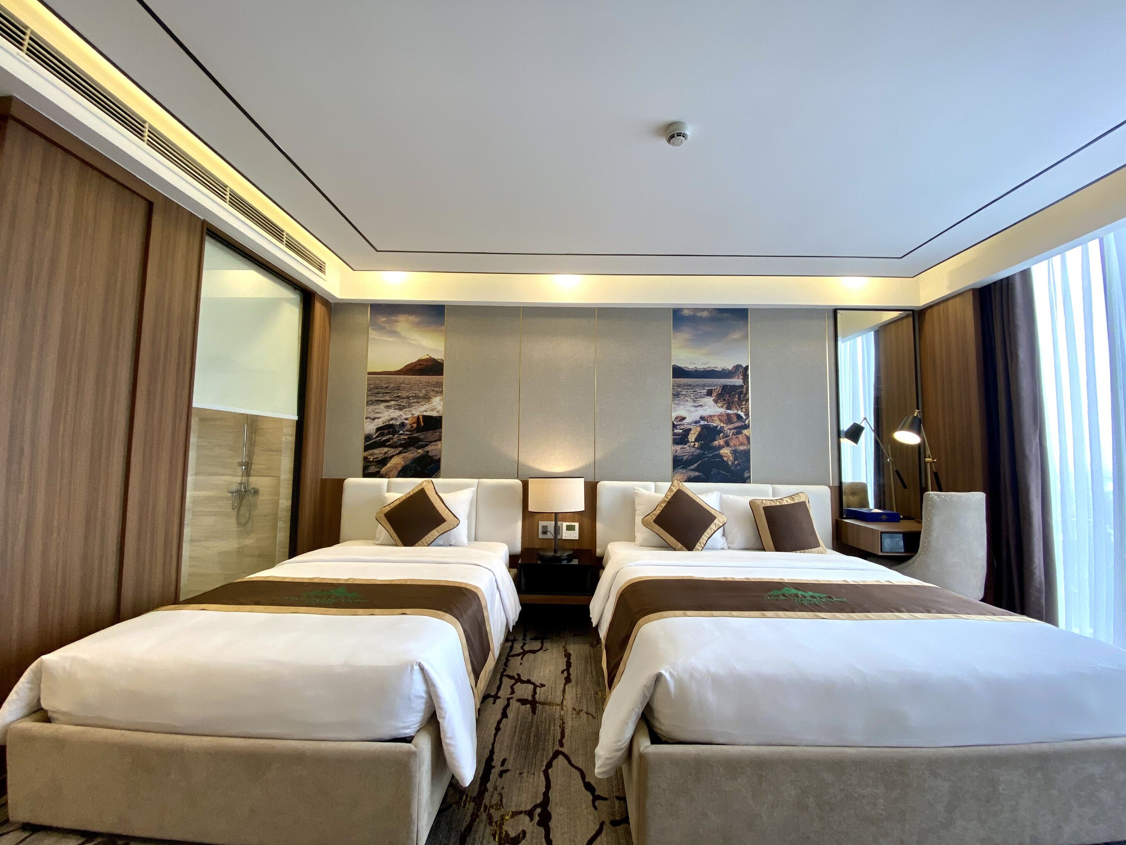 A hotel room with two beds, a large window, and a view of the sea.
