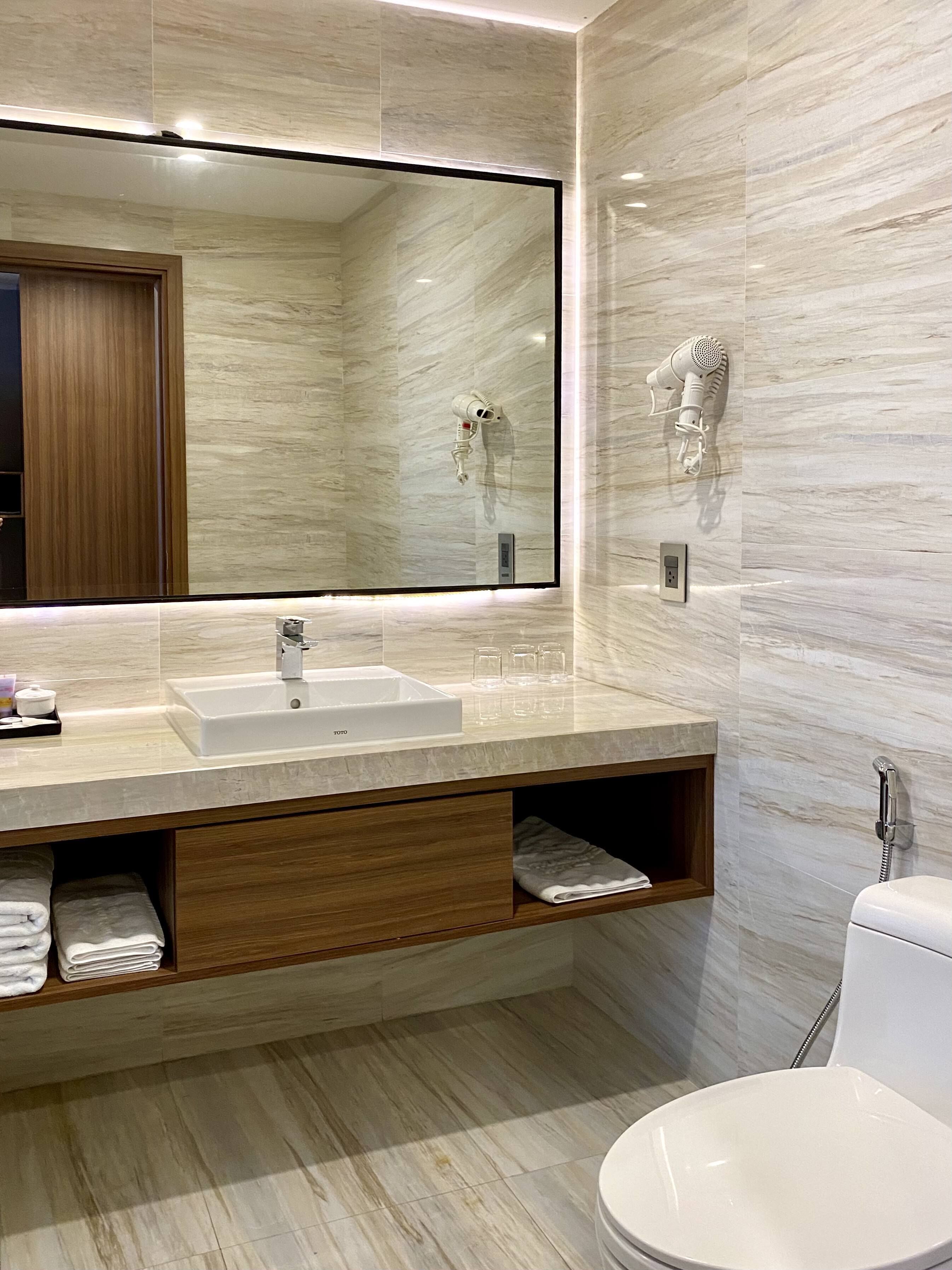 Un baño moderno con un espejo grande, un lavamanos, un secador de pelo y un inodoro.