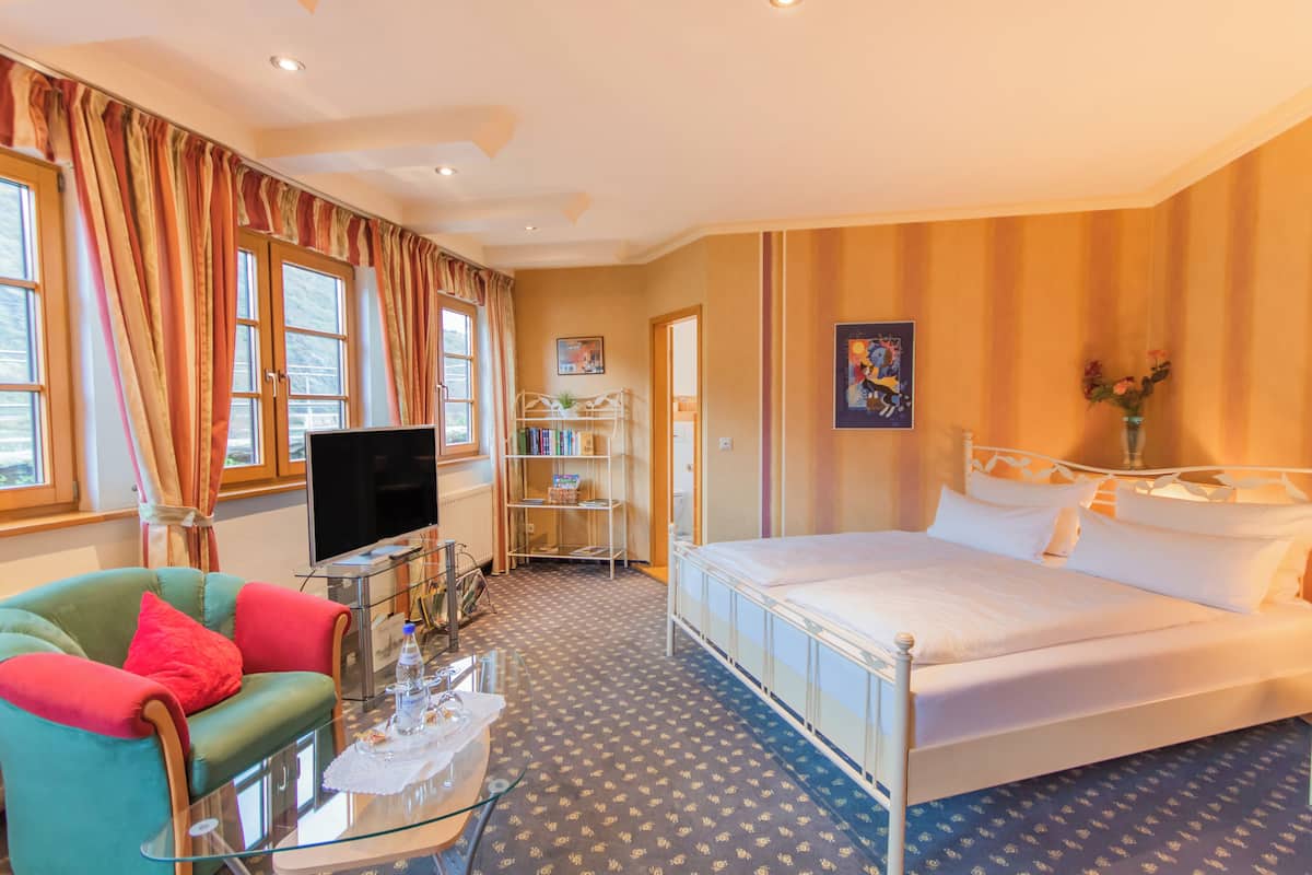 Una habitación de hotel con cama, televisión, mesa de centro de vidrio, sofá y estantería.