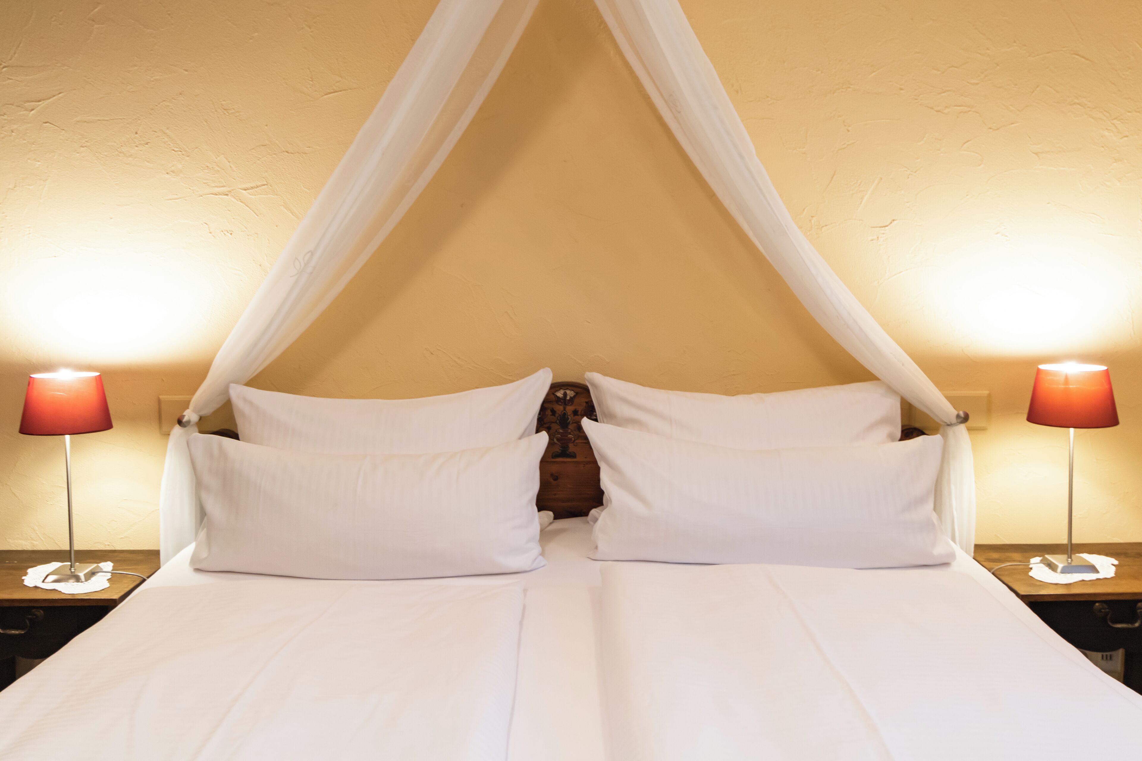 A room with a canopy bed, two bedside lamps, and a wooden nightstand.