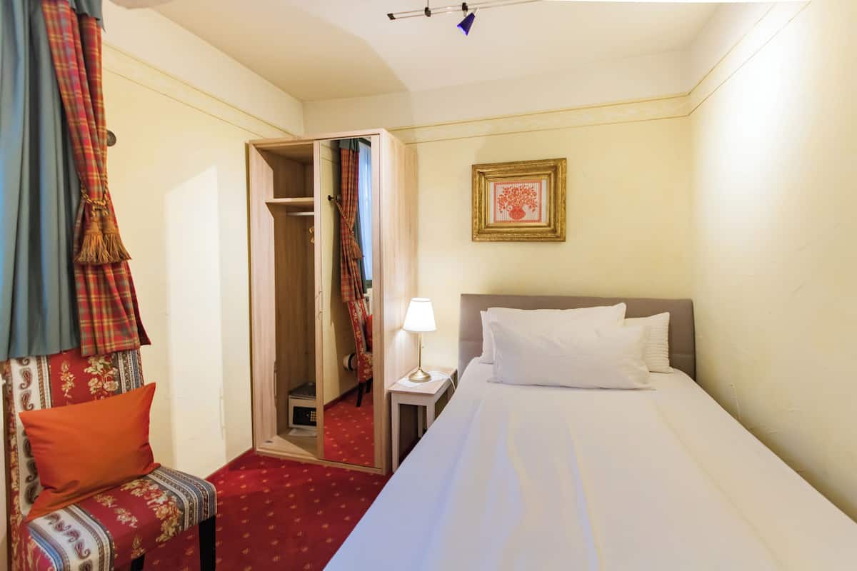 Habitación de hotel con cama, mesita de noche con lámpara, una silla roja con estampado, armario y espejo.