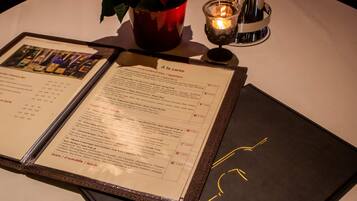A menu with various dishes and prices, a candle, and a red cup with a rose on a table.