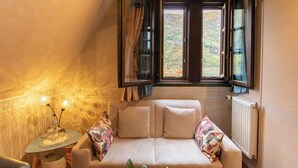 A cozy room with a sofa, a small table with a lamp, and a window with curtains. - Hotel Weiler (Oberwesel)