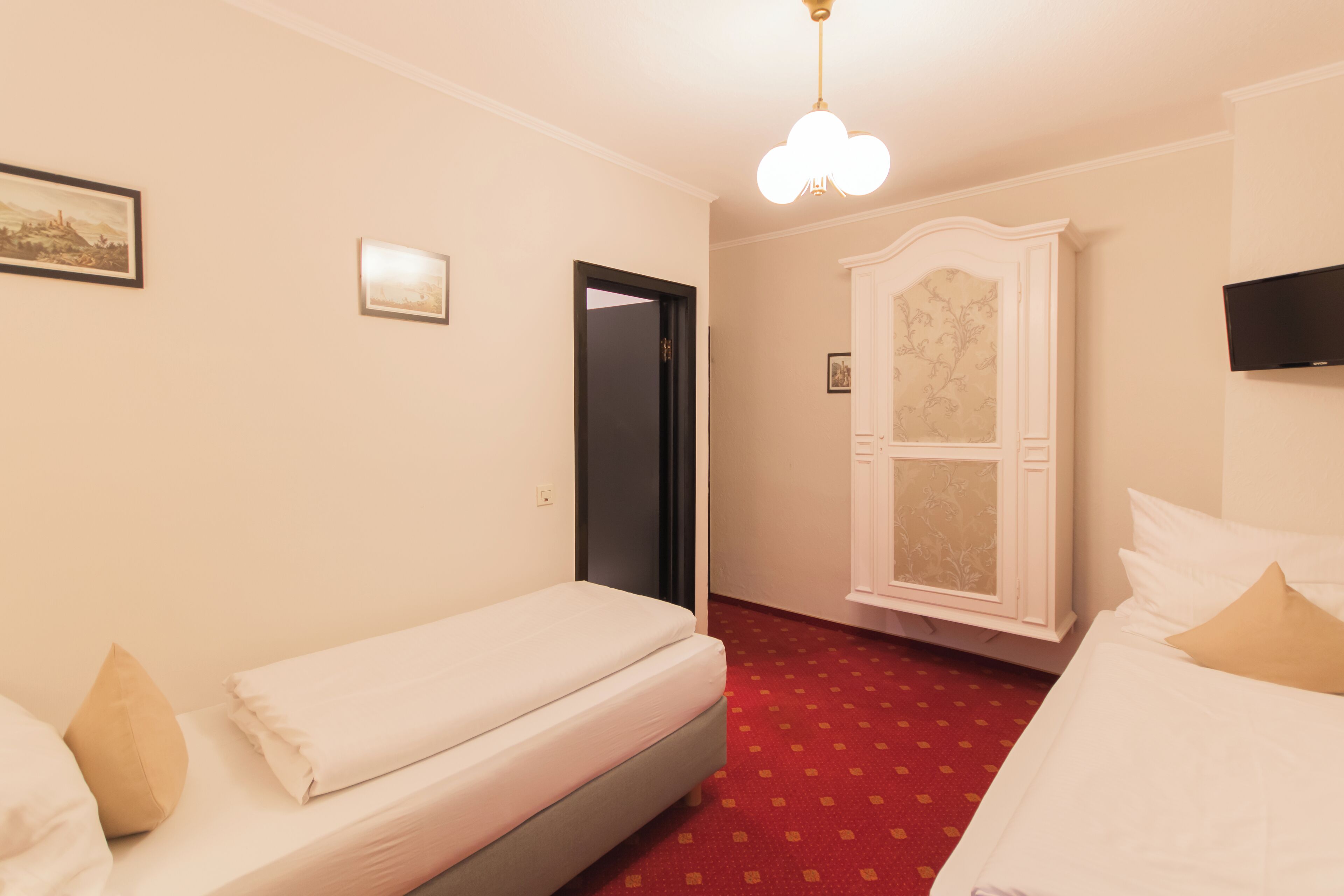 A hotel room with a bed, a wardrobe, a television, and a door leading to another room.