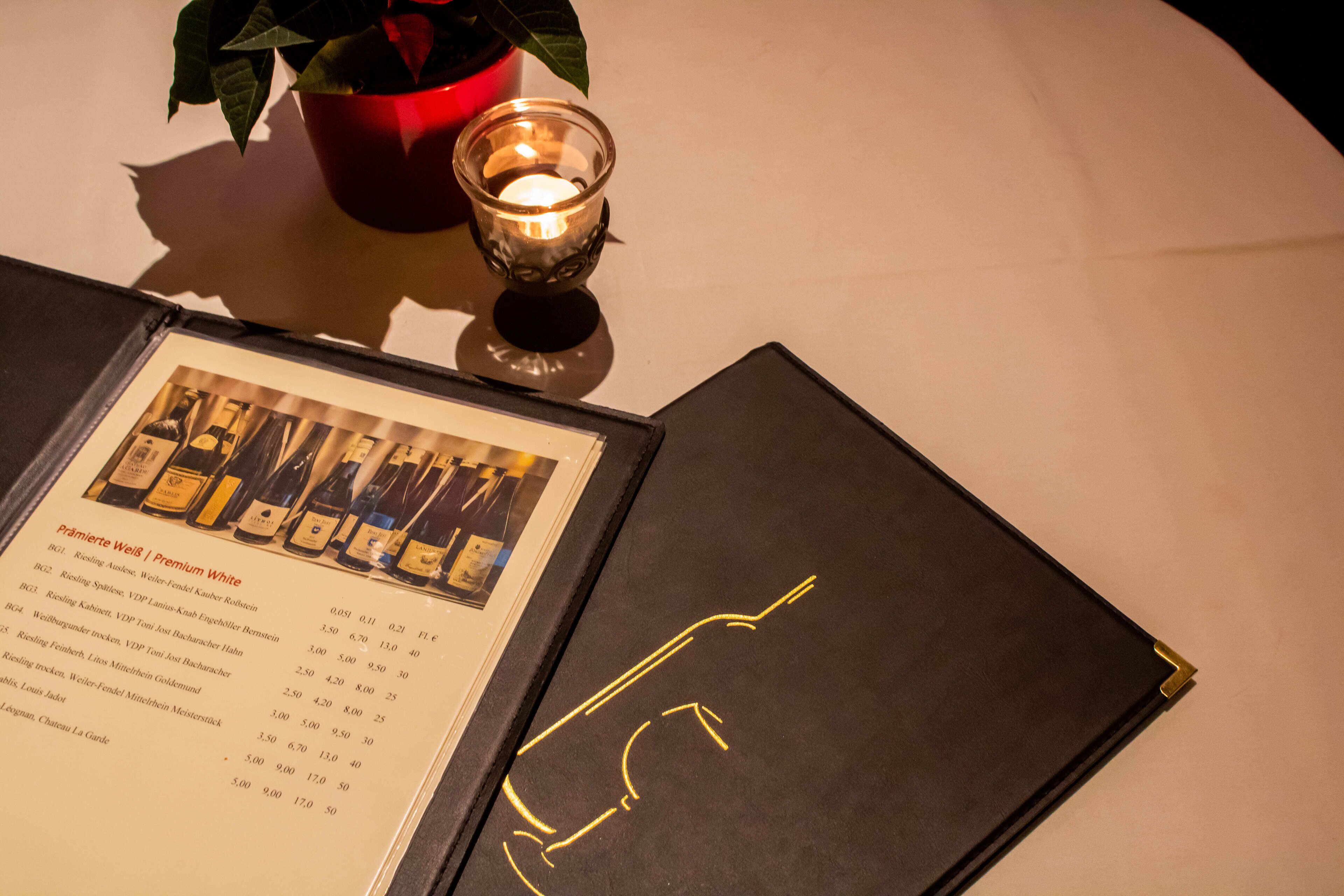 A menu with wine options and a candle on a table.