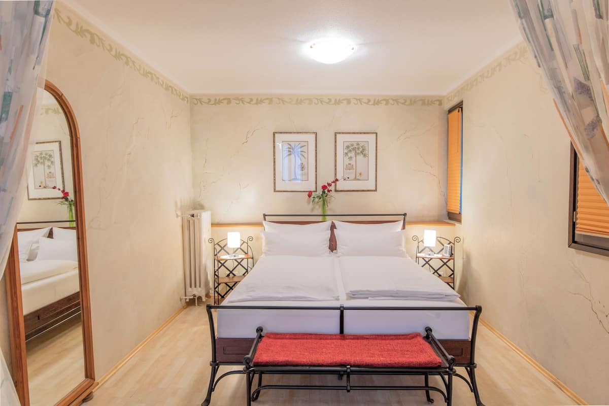 Un dormitorio ordenado con una cama doble, mesitas de noche con lámparas, un espejo y dos cuadros en la pared.