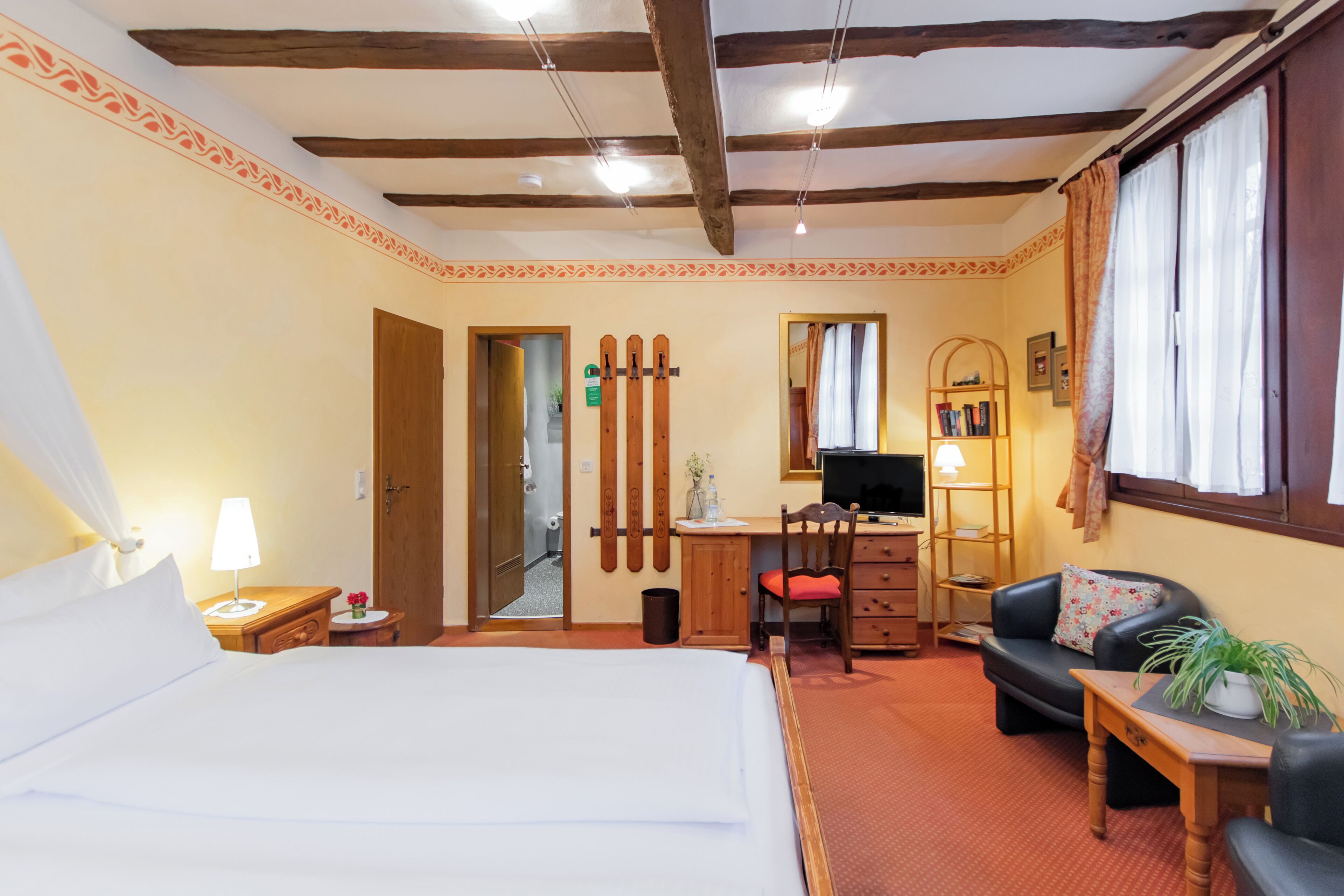 Habitación de hotel con cama, escritorio, silla, sofá, una mesita y ventana con cortinas.
