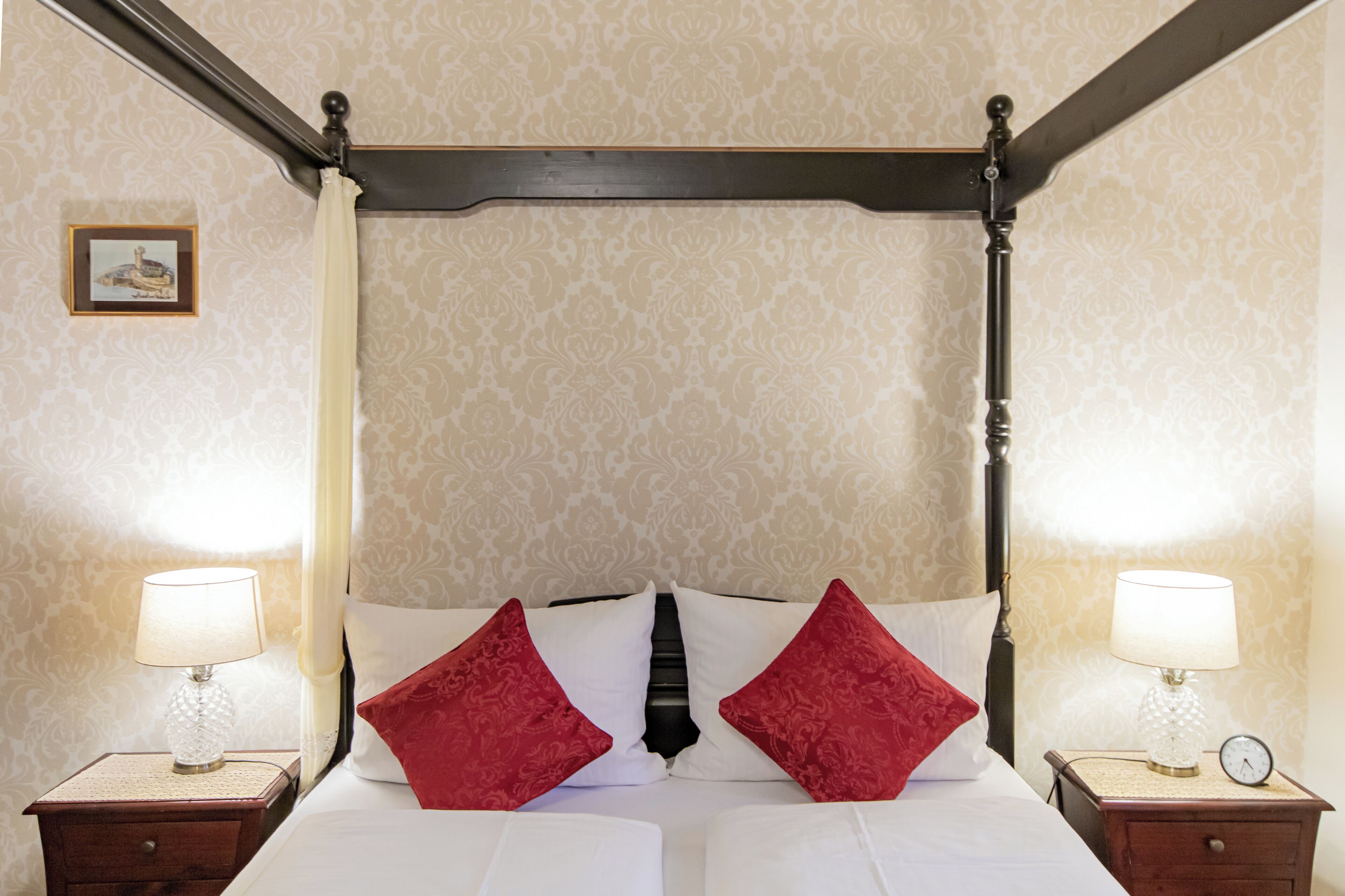 A four-poster bed with two nightstands on either side, each with a lamp and a clock.