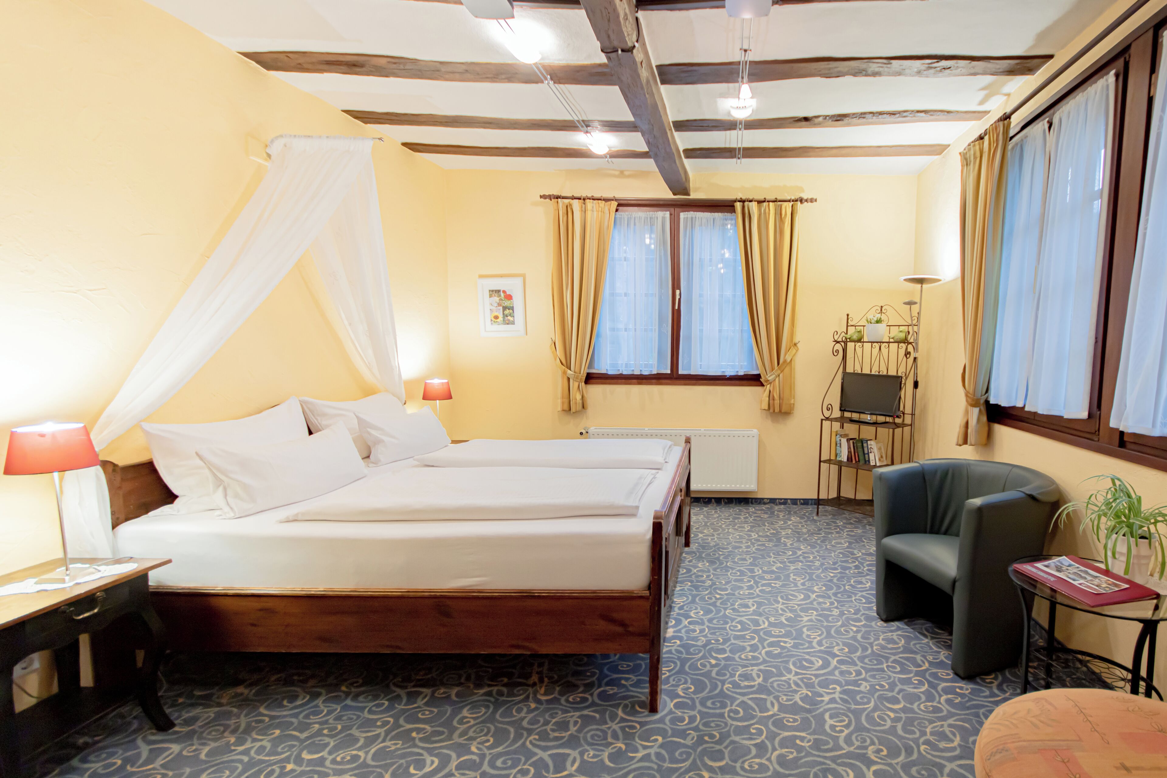 A hotel room with a large bed, a chair, a small table, and a window with curtains.