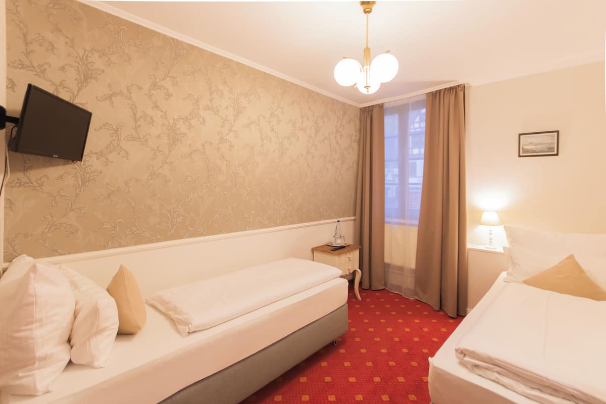 Habitación de hotel con dos camas, un televisor montado en la pared, una mesita de noche, una lámpara y una ventana con cortinas.