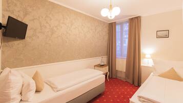A hotel room with two beds, a TV mounted on the wall, a nightstand, a lamp, and a window with curtains.