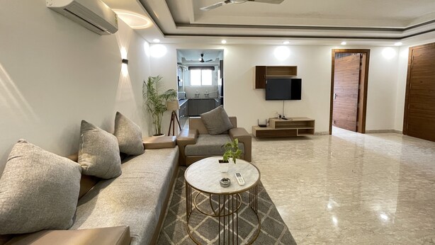 A modern living room with a sofa, coffee table, and a TV mounted on the wall. - BedChambers Serviced Apartments , Ardee City (Gurgaon)