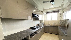 A modern kitchen with a marble countertop, stainless steel appliances, and a window with curtains. - BedChambers Serviced Apartments , Ardee City (Gurgaon)