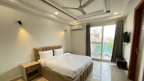 A modern bedroom with a large bed, a ceiling fan, and a view of the outside. - BedChambers Serviced Apartments , Ardee City (Gurgaon)