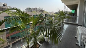 A balcony with potted plants, a white railing, and a view of surrounding buildings. - BedChambers Serviced Apartments , Ardee City (Gurgaon)