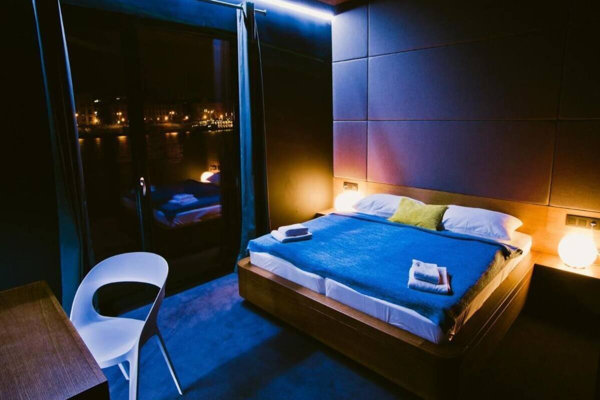 A hotel room with a bed, a white chair, and a view of a cityscape at night.