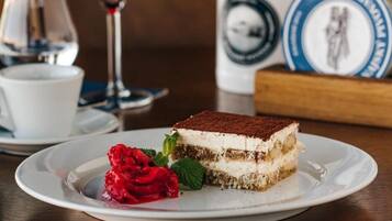Uma fatia de tiramisu em um prato branco, com uma rosa vermelha e folhas de hortelã.