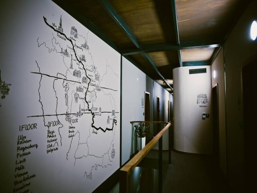 A hallway with a map on the wall, a wooden bench, and a cylindrical air vent.