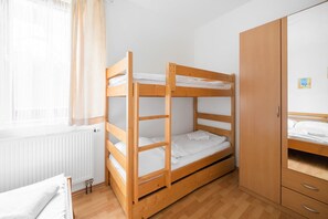 A bunk bed room with a wooden wardrobe and a window with curtains.
