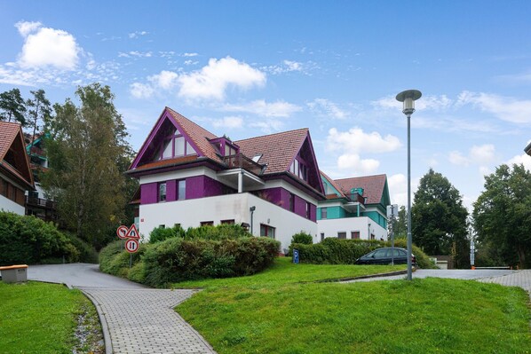 A modern residential building with a sloped roof, a paved driveway, and a parking area.