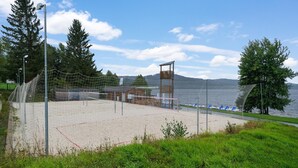Une plage de sable avec un filet de volley-ball, une structure en bois et une vue sur le lac.