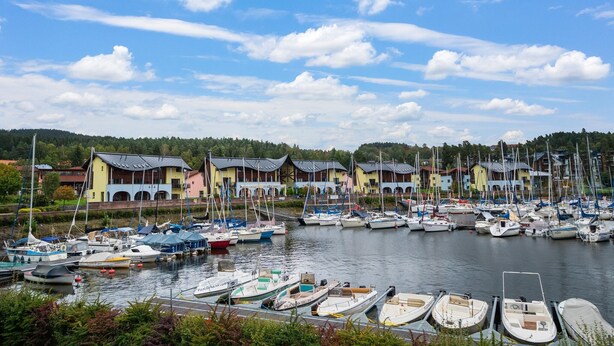 Un port de plaisance où sont amarrés de nombreux bateaux, entouré d’immeubles aux couleurs vives et aux styles architecturaux variés.