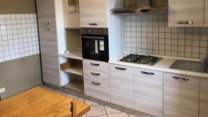 A modern kitchen with light wood cabinets, a black oven, a gas stove, and a stainless steel range hood. - 2 Bedroom Apartment (Bosco Chiesanuova)