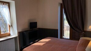 A bedroom with a bed, a television on a stand, a window with curtains, and a view of the outdoors. - 2 Bedroom Apartment (Bosco Chiesanuova)