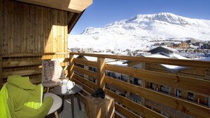 Een houten balkon met uitzicht op een met sneeuw bedekte berg en een stad eronder.