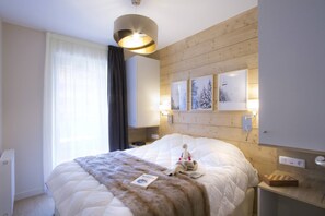 Una habitación de hotel con una cama grande, un cabecero con luces empotradas, una mesita de noche con lámpara y una ventana con cortinas.