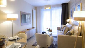 Een moderne hotelkamer met een zithoek, een loungeset, een wandtelevisie en een groot raam met gordijnen.