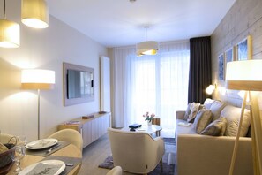 Ein modernes Hotelzimmer mit Essbereich, einer Sofagruppe, einem an der Wand montierten Flachbildfernseher und einem großen Fenster mit Vorhängen.